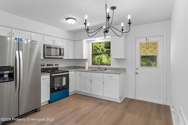 kitchen with stainless steel appliances, sink, white cabinetry, light wood-type flooring, and decorative light fixtures