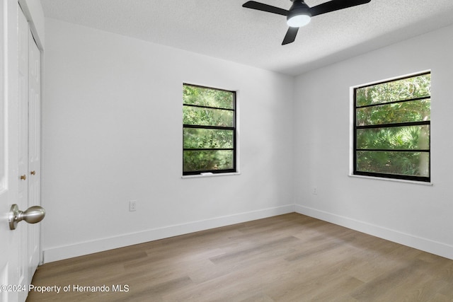 spare room with a textured ceiling, light wood-type flooring, a wealth of natural light, and ceiling fan