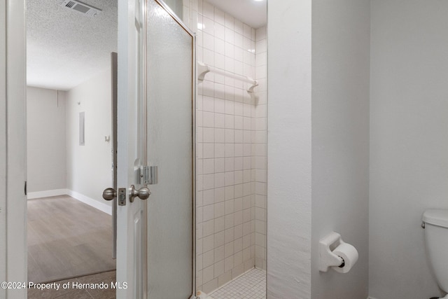 bathroom with wood-type flooring, a textured ceiling, toilet, and an enclosed shower