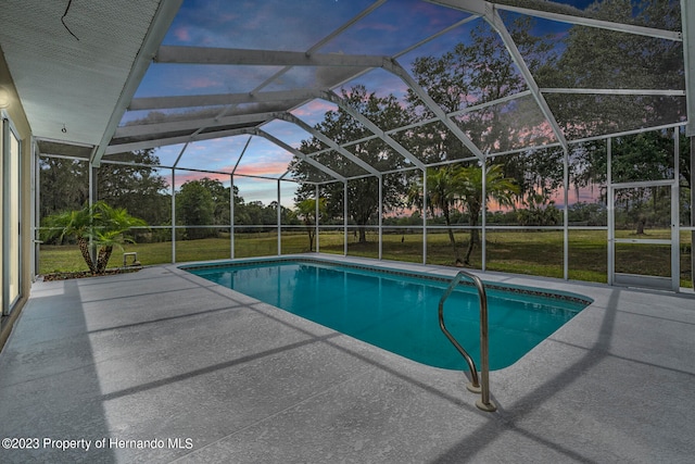 pool at dusk featuring a lawn, a lanai, and a patio