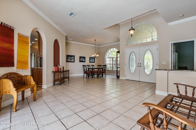 foyer entrance with crown molding, light tile patterned floors, french doors, and a notable chandelier