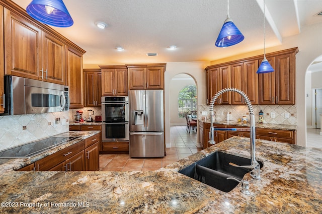 kitchen with pendant lighting, stainless steel appliances, dark stone counters, and sink