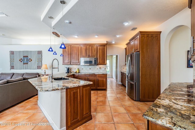 kitchen with decorative backsplash, sink, light stone countertops, pendant lighting, and appliances with stainless steel finishes