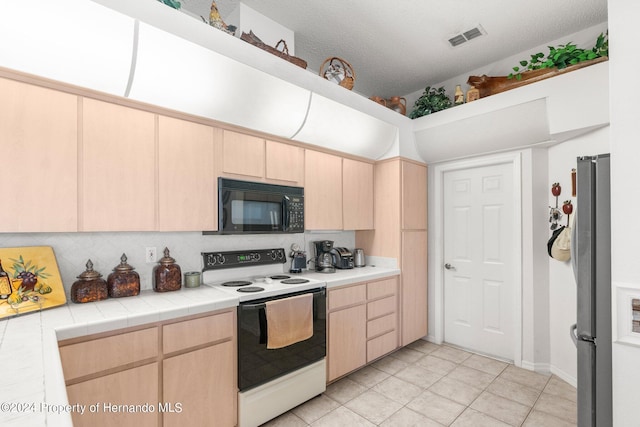 kitchen with tile counters, light brown cabinetry, stainless steel fridge, and electric stove