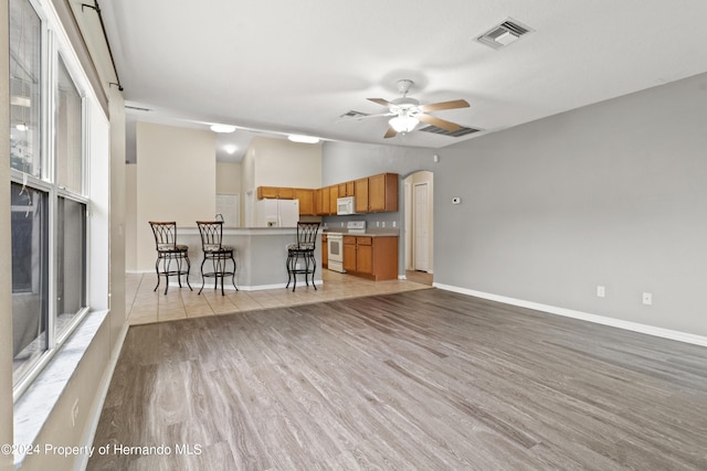 kitchen with vaulted ceiling, a breakfast bar area, ceiling fan, light wood-type flooring, and white appliances