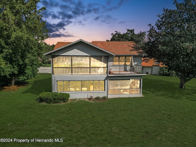 back house at dusk featuring a lawn and a balcony