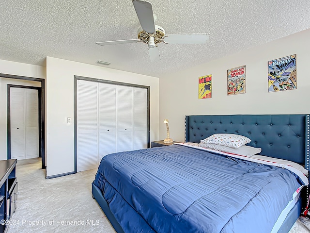 bedroom featuring a closet, a textured ceiling, light colored carpet, and ceiling fan