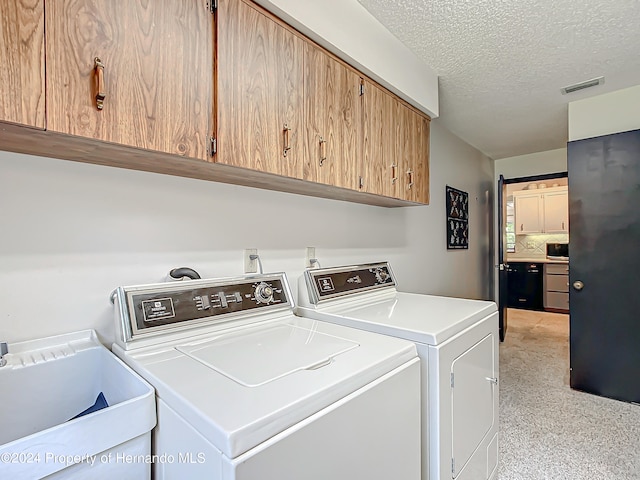 washroom with a textured ceiling, cabinets, sink, and washing machine and clothes dryer