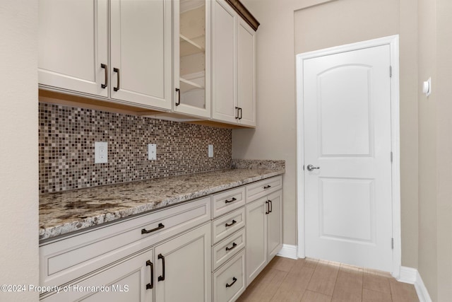 kitchen with white cabinets, light stone countertops, light hardwood / wood-style floors, and decorative backsplash