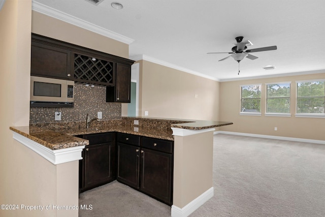 kitchen with dark stone counters, backsplash, kitchen peninsula, and light carpet