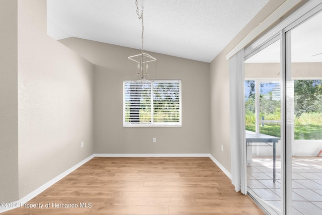 unfurnished dining area with a textured ceiling, light hardwood / wood-style floors, lofted ceiling, and an inviting chandelier