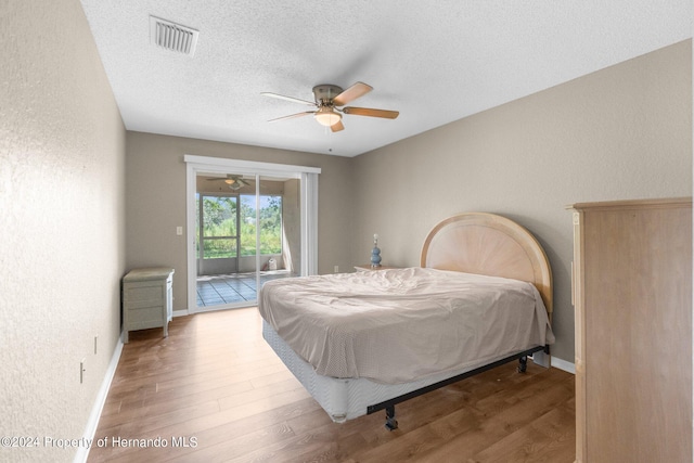 bedroom with access to exterior, ceiling fan, hardwood / wood-style floors, and a textured ceiling