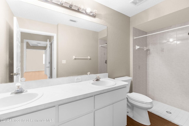 bathroom with hardwood / wood-style floors, vanity, toilet, a textured ceiling, and a tile shower