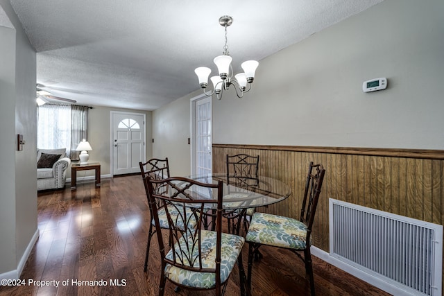 dining room with dark hardwood / wood-style flooring, wooden walls, a textured ceiling, and ceiling fan with notable chandelier