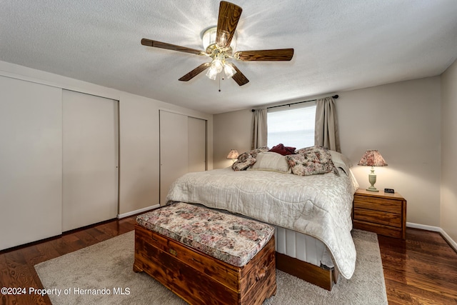 bedroom with dark wood-type flooring, ceiling fan, a textured ceiling, and two closets