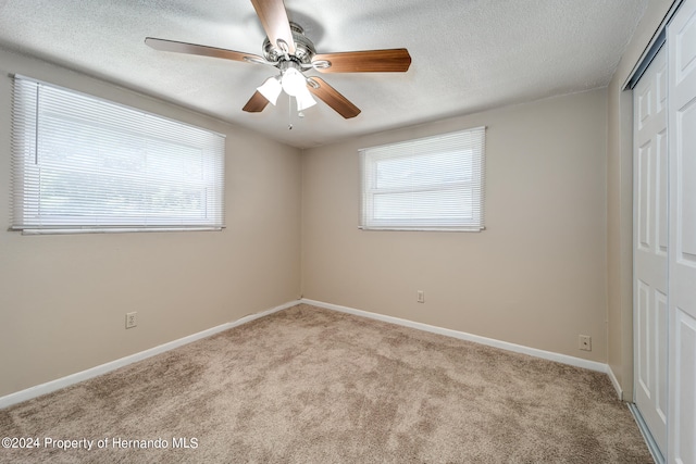 unfurnished bedroom with a textured ceiling, light colored carpet, ceiling fan, and a closet