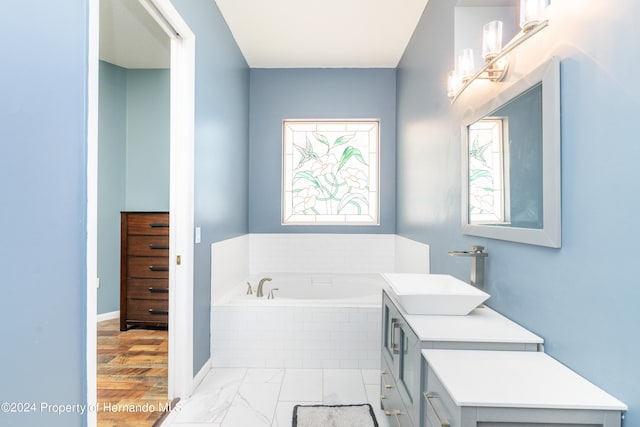 bathroom with hardwood / wood-style floors, vanity, and tiled tub