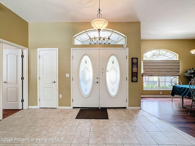 entryway with light hardwood / wood-style floors, a textured ceiling, an inviting chandelier, and french doors