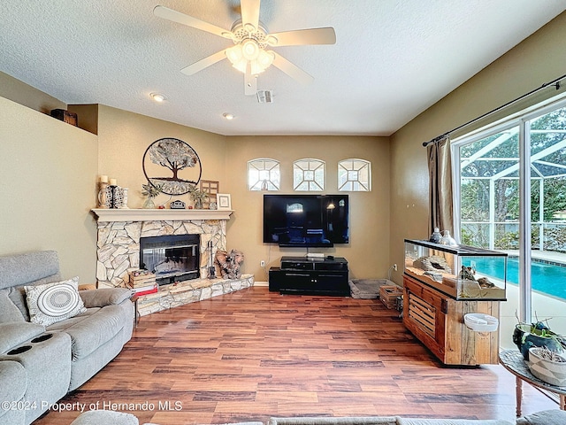 living room featuring a textured ceiling, a fireplace, wood-type flooring, and ceiling fan