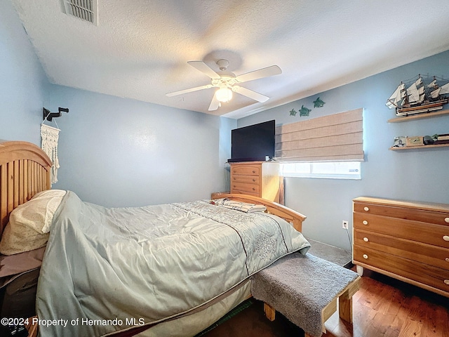 bedroom with ceiling fan, a textured ceiling, and dark hardwood / wood-style flooring