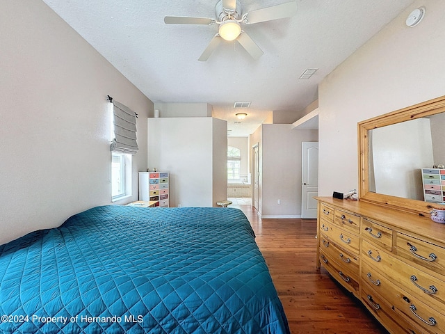 bedroom with dark wood-type flooring, a textured ceiling, ceiling fan, and ensuite bath