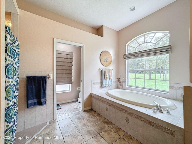 bathroom featuring toilet, a relaxing tiled tub, a textured ceiling, and tile patterned floors