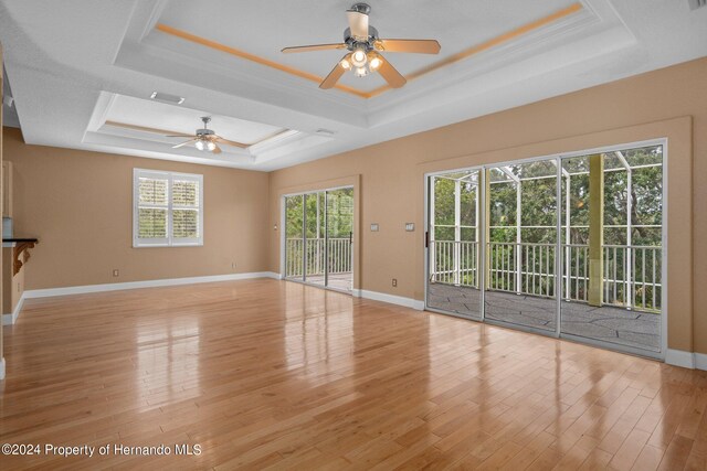 unfurnished living room with light wood-type flooring, crown molding, ceiling fan, and a raised ceiling