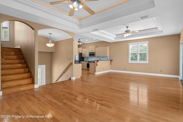 unfurnished living room featuring a wealth of natural light, a tray ceiling, crown molding, and light hardwood / wood-style flooring