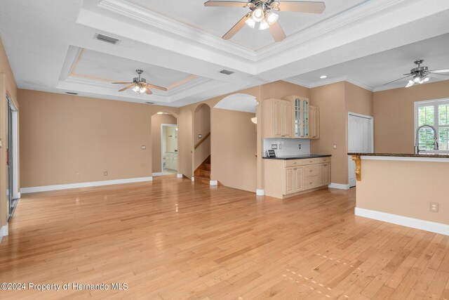 unfurnished living room with ceiling fan, a raised ceiling, light wood-type flooring, and crown molding