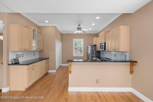 kitchen with stainless steel appliances, kitchen peninsula, dark stone counters, ceiling fan, and light hardwood / wood-style flooring