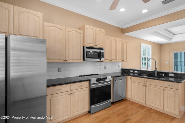 kitchen with dark stone counters, light hardwood / wood-style flooring, sink, ornamental molding, and appliances with stainless steel finishes