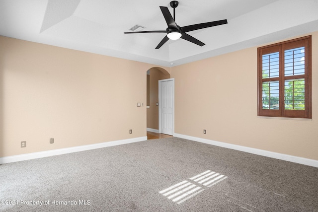 empty room with ceiling fan, a raised ceiling, and carpet floors