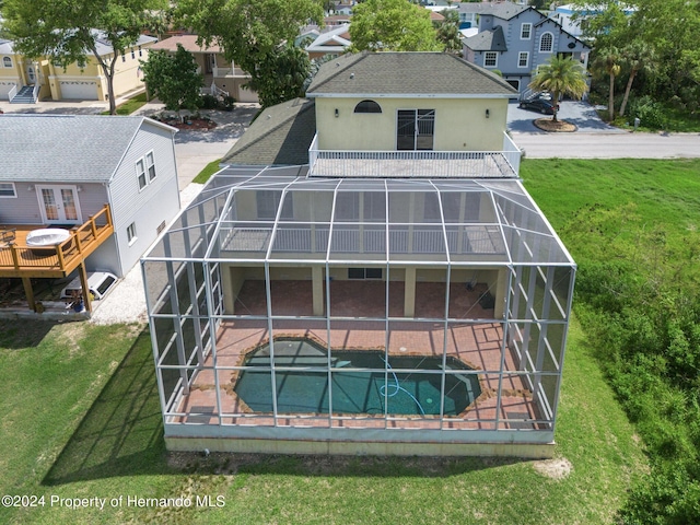 rear view of house featuring a swimming pool with hot tub, glass enclosure, a patio, and a balcony