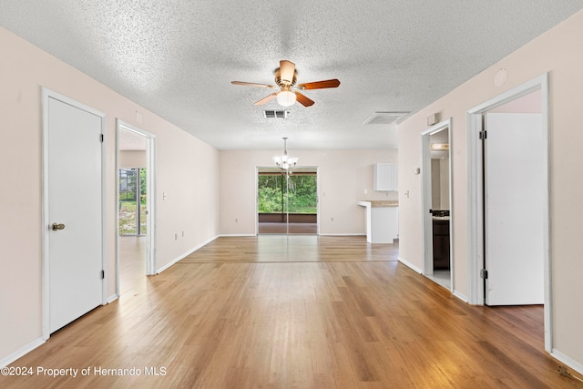 unfurnished living room with a wealth of natural light, ceiling fan with notable chandelier, a textured ceiling, and light wood-type flooring