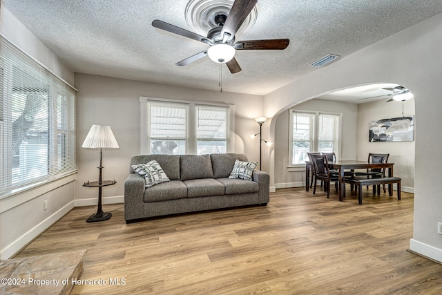 living room with a textured ceiling, light hardwood / wood-style floors, and ceiling fan