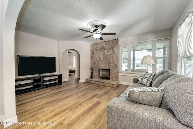 living room featuring a fireplace, hardwood / wood-style flooring, ceiling fan, and a textured ceiling