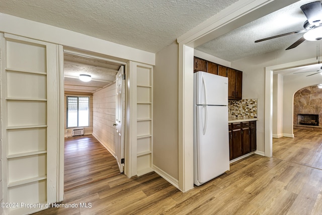 kitchen with light hardwood / wood-style floors, a textured ceiling, a fireplace, dark brown cabinets, and white refrigerator