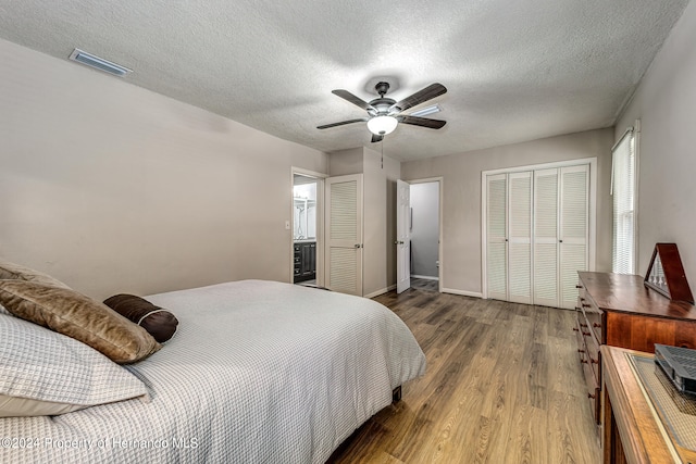 bedroom with ceiling fan, ensuite bath, wood-type flooring, and a textured ceiling