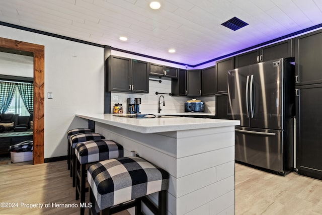 kitchen featuring kitchen peninsula, a kitchen breakfast bar, stainless steel refrigerator, backsplash, and light wood-type flooring