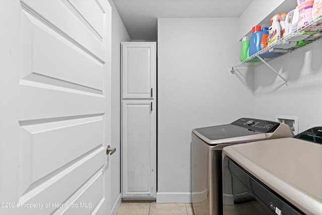 clothes washing area featuring cabinets, light tile patterned flooring, and washing machine and clothes dryer