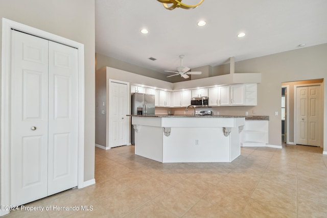 kitchen with a center island with sink, stainless steel appliances, white cabinetry, light tile patterned floors, and a kitchen breakfast bar