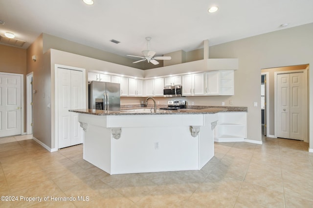 kitchen featuring dark stone counters, white cabinetry, appliances with stainless steel finishes, and a kitchen island with sink