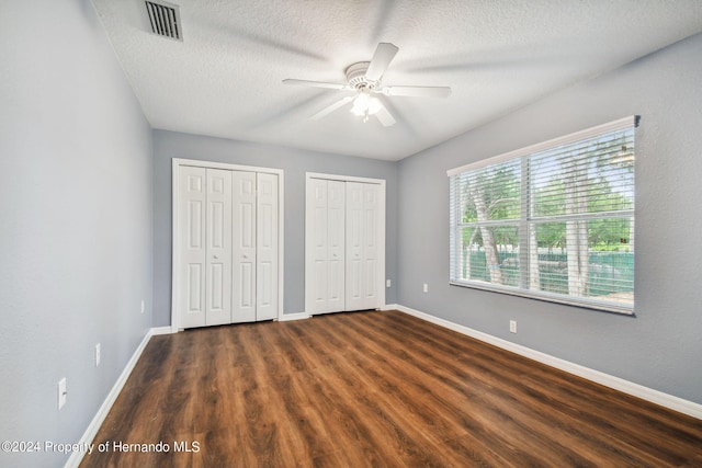 unfurnished bedroom with ceiling fan, dark hardwood / wood-style floors, a textured ceiling, and two closets