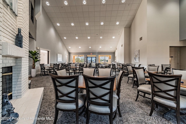 carpeted dining room with a brick fireplace and a high ceiling