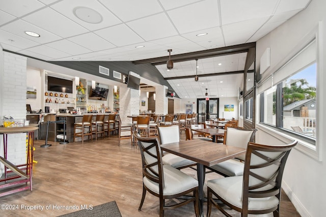 dining space featuring lofted ceiling with beams, bar, and hardwood / wood-style flooring