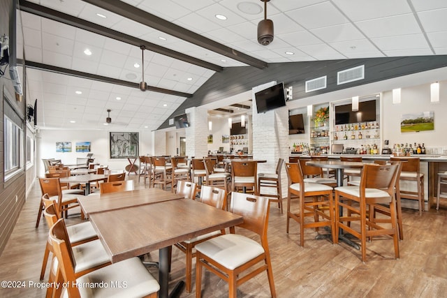 dining room featuring bar area, light wood-type flooring, and vaulted ceiling with beams