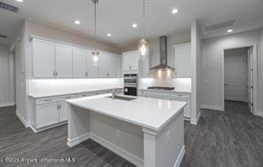 kitchen with a center island with sink, white cabinetry, decorative light fixtures, sink, and wall chimney exhaust hood