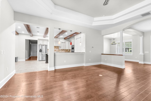 unfurnished living room with beamed ceiling, an inviting chandelier, hardwood / wood-style flooring, and ornate columns