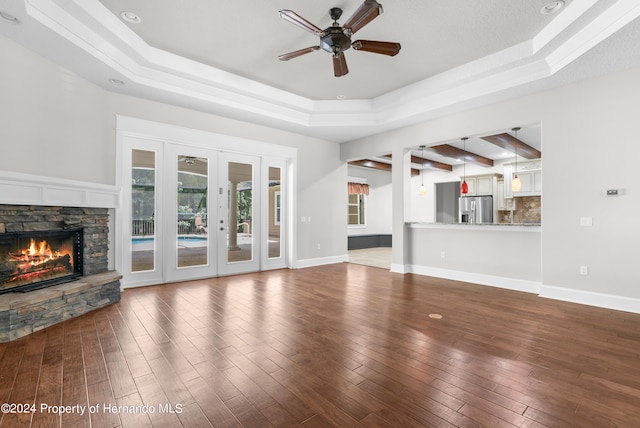 unfurnished living room with french doors, a fireplace, hardwood / wood-style floors, a tray ceiling, and ceiling fan