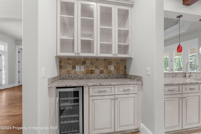 bar with light stone counters, tasteful backsplash, pendant lighting, light wood-type flooring, and wine cooler